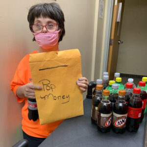 a PELS client wearing a face mask and holding an envelope labeled 'pop money'